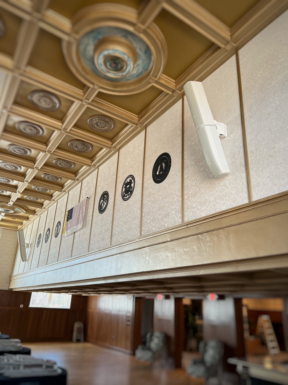 Wall mounted commercial speakers installed in a banquet hall with ornate ceilings