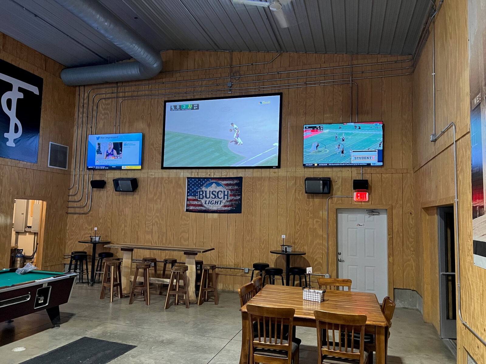 Three large televisions mounted on the wall of a bar and game room