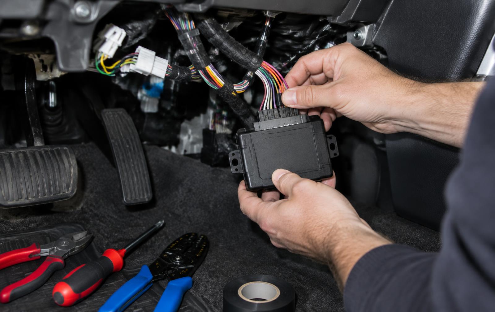 Installer wiring a remote starter module under a vehicle dashboard