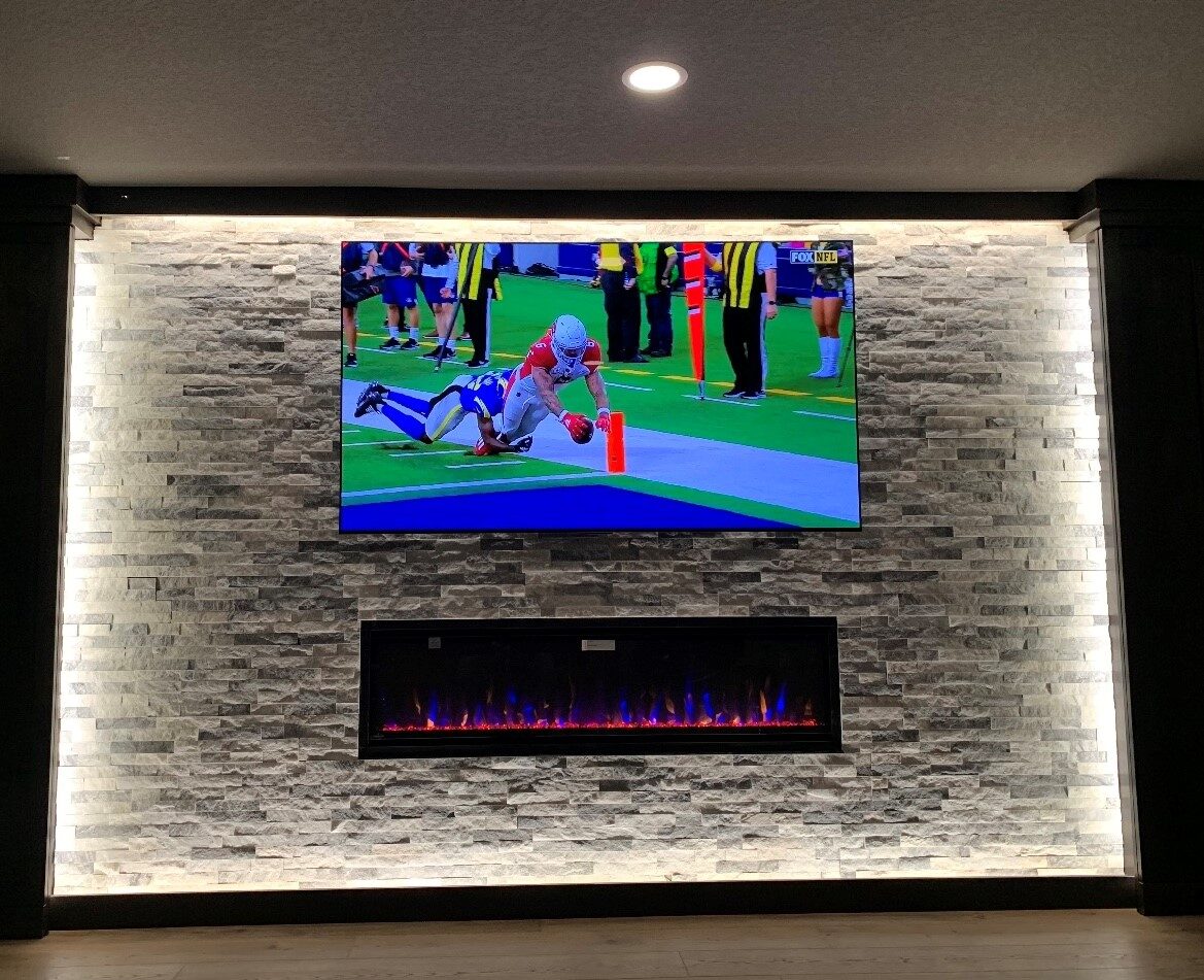 Large television mounted on a stacked stone fireplace wall with accent lighting in an Iowa home
